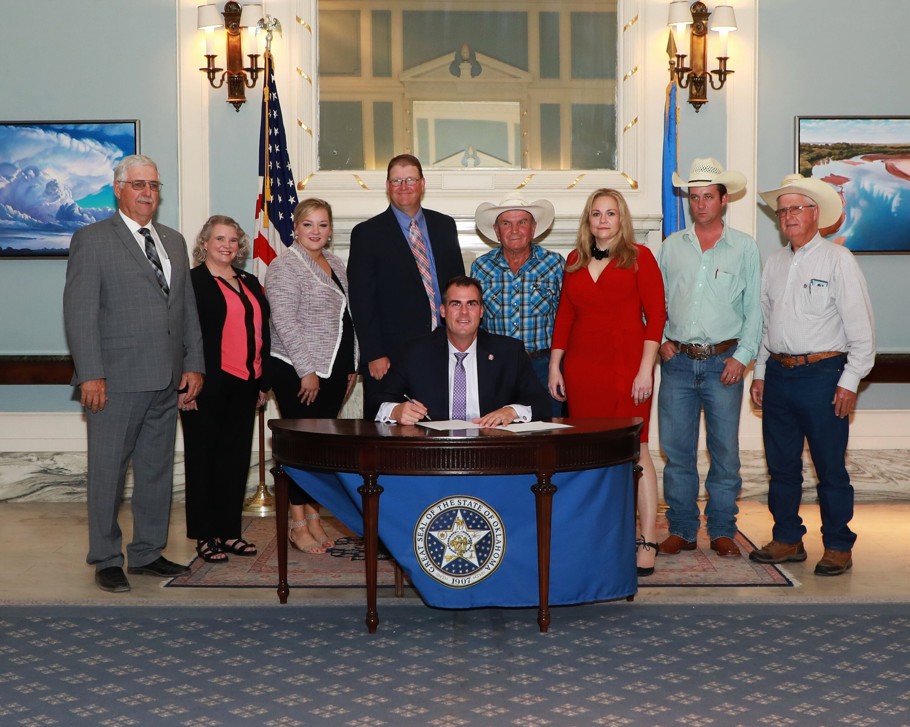 A ceremonial bill signing was also held for SB 543, updating the statutory definition of “feral swine.”  Pictured from left to right are Sen. Roland Pederson, Teena Gunter, Oklahoma Dept. of Agriculture, JanLee Rowlett, Agriculture Department, Jeramy Rich, lobbyist, Dale Toon, Wild Boar Ridge Hunting Ranch owner, Michelle Sutton, lobbyist, Kane Webb, rancher, Bryan Rickman, heritage hog rancher, and Gov. Kevin Stitt, seated.
